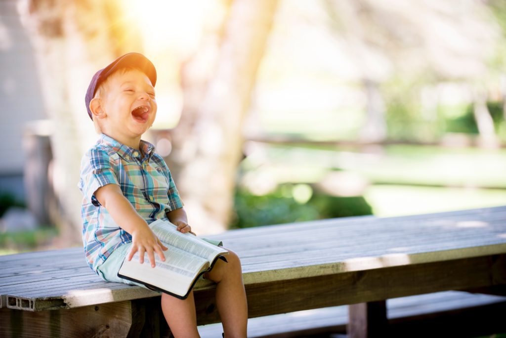 Photo of a child sitting with a Bible and laughing.