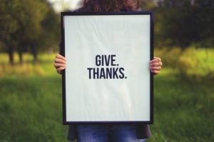 Person holding up sign that says give thanks.